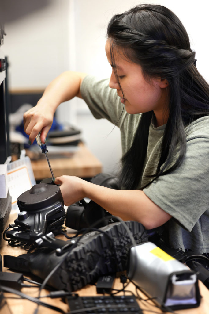 Man I (Maggie) Wu uses a screwdriver while setting up the ankle exoskeleton on a bench top.